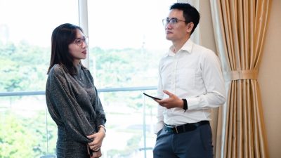 Two colleagues engaged in a business conversation indoors with a window view.