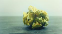 A close-up of a crumpled yellow paper ball with handwriting on a wooden surface.