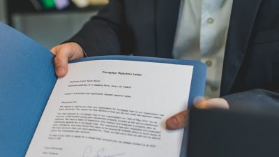 Close-up view of a person holding a mortgage rejection letter in a folder, indoors.