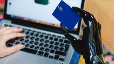Person with prosthetic hand using laptop for online shopping, holding a credit card.