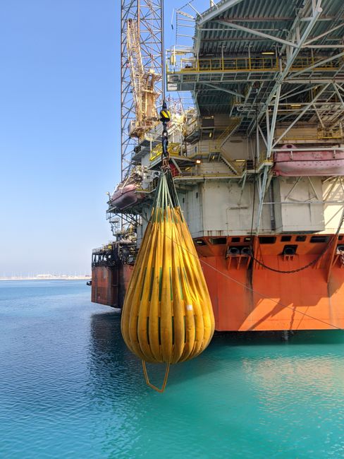 Offshore platform featuring a yellow water load bag for crane testing above the ocean.