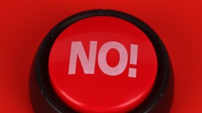 Close-up of a red button with "NO" text, set on a vivid red background. Ideal for concepts of denial or negativity.