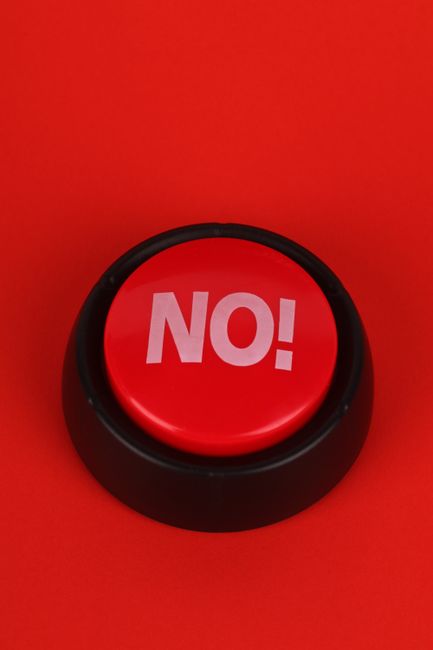 Close-up of a red button with "NO" text, set on a vivid red background. Ideal for concepts of denial or negativity.