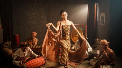 Indonesian woman dances with musicians, wearing traditional attire in a cultural performance.