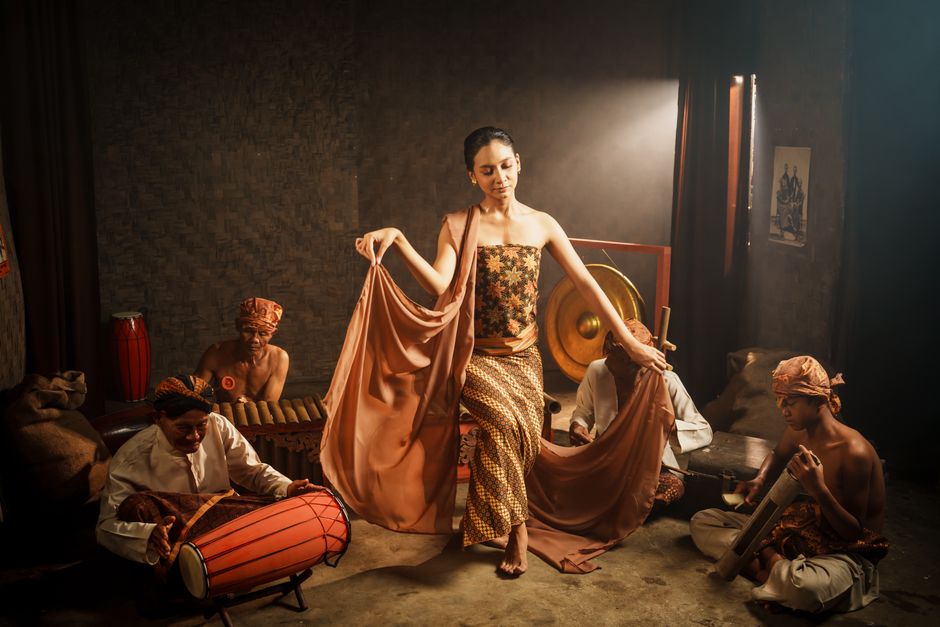 Indonesian woman dances with musicians, wearing traditional attire in a cultural performance.