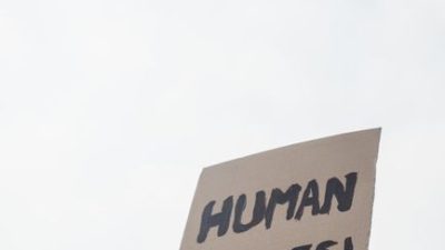 A close-up of a human rights protest sign held up against the sky.
