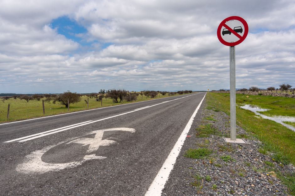 Deserted rural road with a no overtaking sign under cloudy skies and vast landscape.