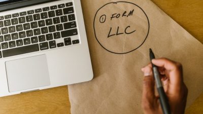 Close-up of hand writing 'Form LLC' on craft paper beside a laptop, indicating business planning.
