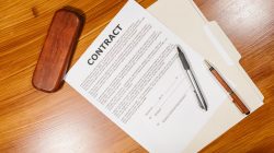 High-angle view of a contract document with pens and a case on a wooden table.