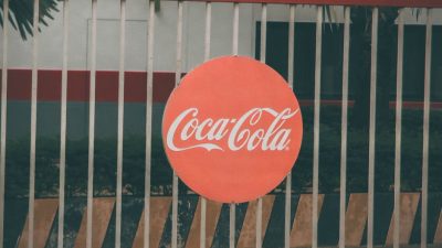 Coca-Cola logo prominently displayed on outdoor fence, urban setting.