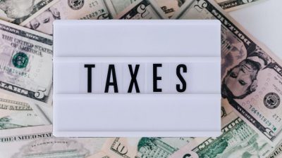 Top view of white vintage light box with TAXES inscription placed on stack of USA dollar bills on white surface