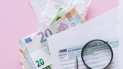 A collection of financial papers, including euro notes, tax return forms, and receipts on a pink surface.
