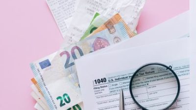 A collection of financial papers, including euro notes, tax return forms, and receipts on a pink surface.